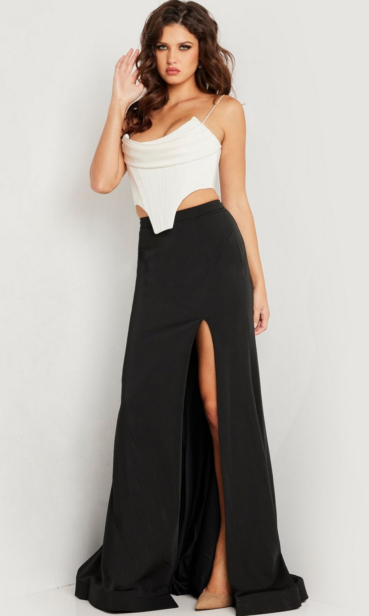 A woman stands against a plain background wearing the Jovani Long Prom Dress 37234, featuring a white corset-style top paired with a long fitted black skirt with a high slit.